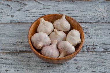 Tahta bir masanın üzerinde sarımsak soğanları olan ahşap bir kase.