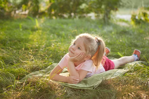 草の上に横たわる小さな幸せな女の子 夏季には庭園で 夢のような — ストック写真