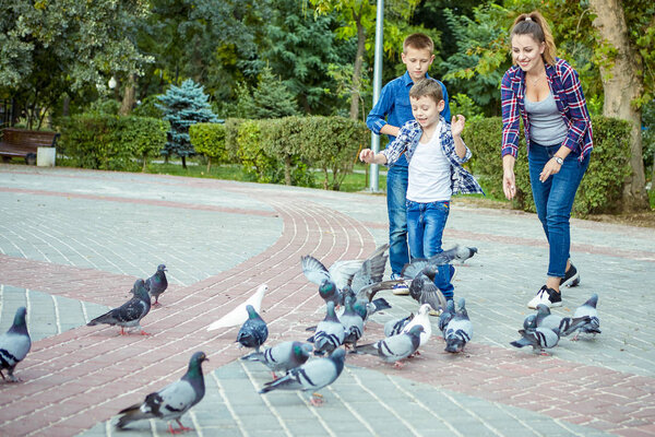 Young beautiful mother and her two sons enjoying together fed pigeons. Happy family. Positive human emotions, feelings, joy.