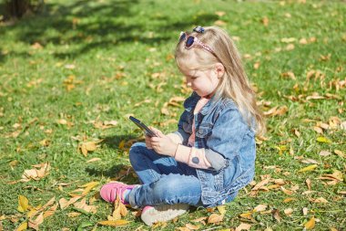 Hareket eden telefon ile küçük kız. Çimenlerin üzerinde oturan smartphone, elinde.