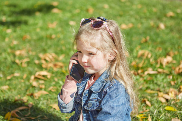 Девочка с мобильным телефоном. Она держит смартфон, сидит на траве
.