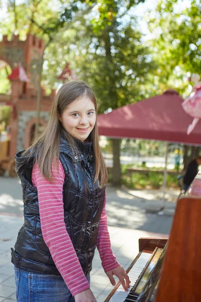 Chica con síndrome de Down tocando el piano al aire libre . — Foto de Stock