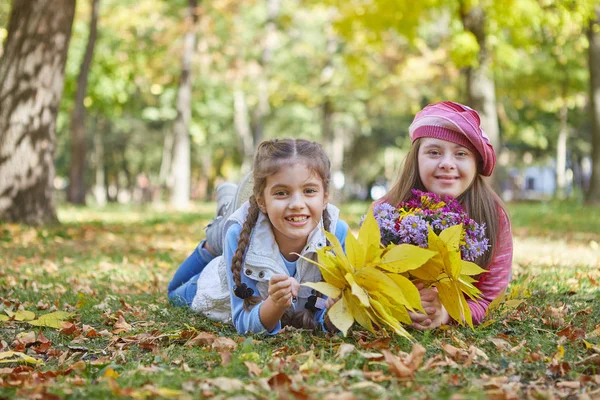 Menina com síndrome de Down e menina no parque de outono . — Fotografia de Stock