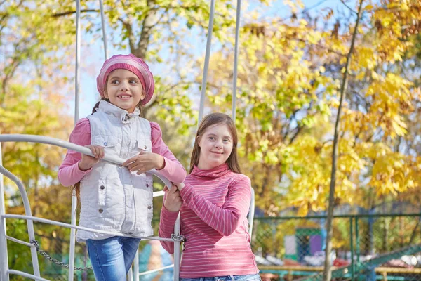 Dziewczyna z zespołem Downa i mała dziewczynka w jesiennym parku. — Zdjęcie stockowe