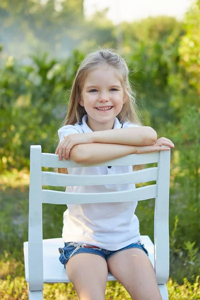 Little Urocza Dziewczyna Siedzi Białym Krześle Ogrodzie Letnim — Zdjęcie stockowe