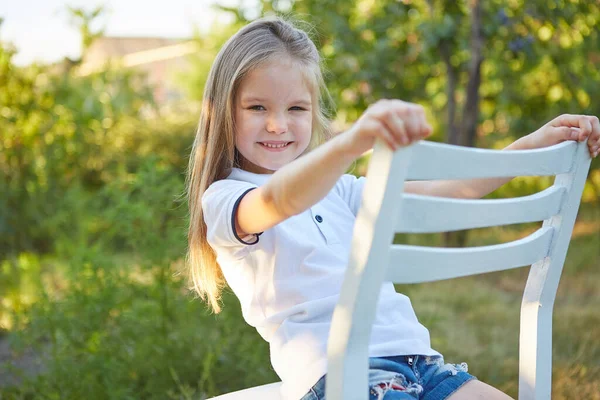 Little Urocza Dziewczyna Siedzi Białym Krześle Ogrodzie Letnim — Zdjęcie stockowe