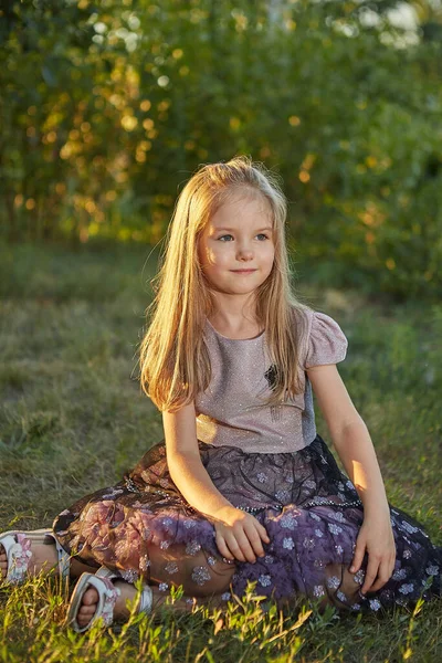 夏天的花园里 一个迷人的小女孩坐在草地上 夕阳西下 — 图库照片