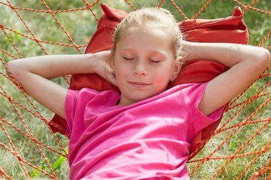 Küçük kız, güneşli bir yaz gününde hasır bir hamakta yatıyor..