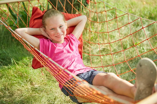小さな女の子は 夏の晴れた日に庭のウィッカーハンモックに横たわっています — ストック写真