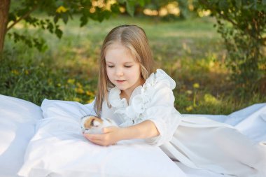 Küçük kız, yaz bahçesinde kedi yavrusuyla yatakta yatıyor.