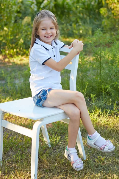 Küçük Sevimli Kız Yaz Bahçesinde Beyaz Bir Sandalyede Oturuyor — Stok fotoğraf