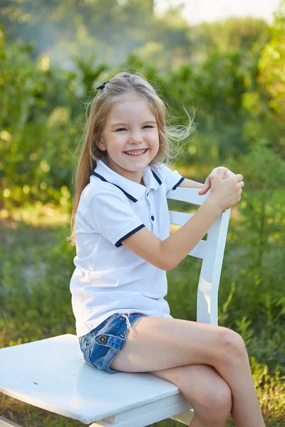 Küçük Sevimli Kız Yaz Bahçesinde Beyaz Bir Sandalyede Oturuyor — Stok fotoğraf