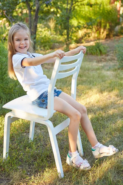 Μικρή Γοητευτική Κοπέλα Κάθεται Μια Λευκή Καρέκλα Στον Καλοκαιρινό Κήπο — Φωτογραφία Αρχείου