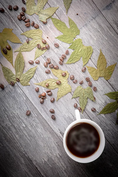 Tazza di caffè e caffè in grani e foglie secche sul tavolo di legno — Foto Stock