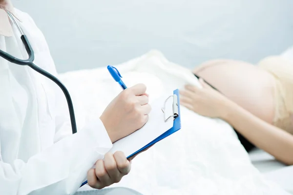 Doktor interakce těhotné ženy ležící na posteli na klinice — Stock fotografie