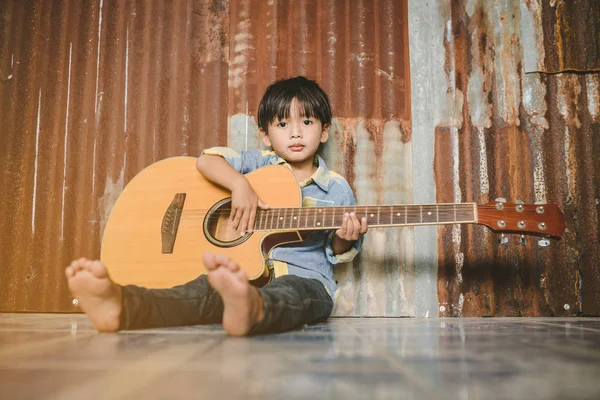 Азиатский мальчик играет на акустической гитаре со стальным фоном — стоковое фото