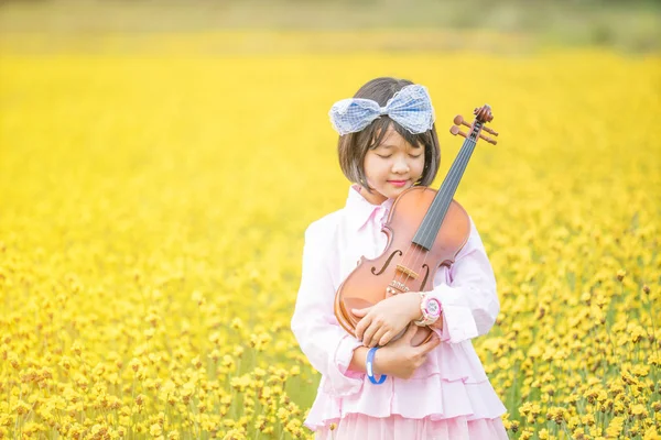 黄色の花畑でバイオリンを弾くかわいい女の子 — ストック写真