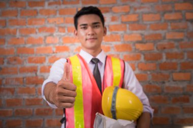 Tuğla ile başparmak gösteren planları ile Asyalı mühendis adam 