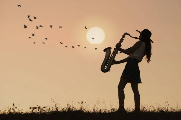 Mujer tocando saxofón con puesta de sol o fondo de salida del sol —  Fotos de Stock