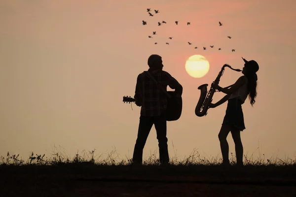 Músico tocar la guitarra y el saxofón con puesta de sol o salida del sol backgr —  Fotos de Stock