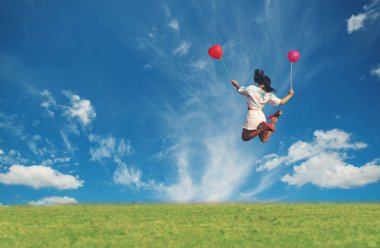 Mutlu kadın yeşil çimlerde renkli balonlarla zıplıyor.