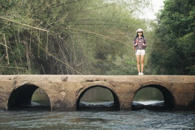 Backpacker kadın doğa arka plan ile eski köprü üzerinde duran