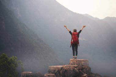 Sırt çantalı kadın dağın tepesinde duruyor ve kollarını açıyor.