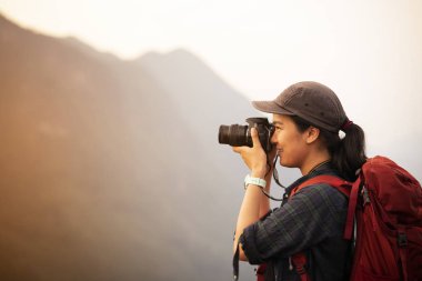 Sırt çantalı kadın dağın zirvesinde fotoğraf çekiyor.