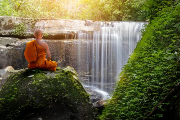 Buda keşişi şelaleyle meditasyon yapıyor.