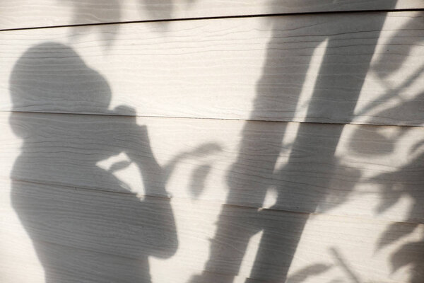 Sunny evening background, shadow of people and leaf on white wall of the house, silhouette woman take photo lonely