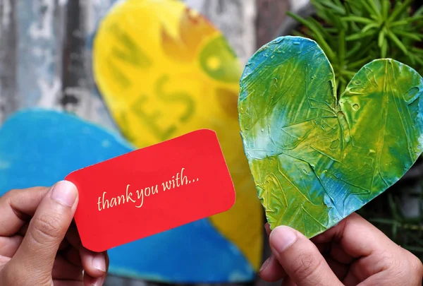 Thank you background with human hand hold the red note paper with  thank you with love message , shape heart and green plant at bottom