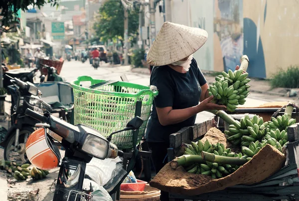 Vietnamita mulher stand considerar bananas no carrinho na beira da estrada — Fotografia de Stock