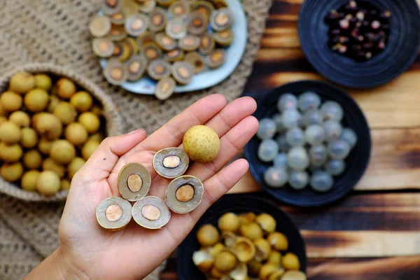 Longan fruits dans la main des gens avec des graines noires, écorce jaune, coupé i — Photo