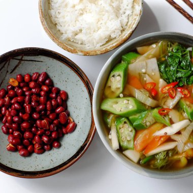 Vietnamlı vejetaryen mutfağı, beyaz arka planda günlük aile yemeği, domatesli sebze çorbası, bambu filizi, su ıspanağı, soya soslu kızarmış fıstık ve öğle yemeği için pirinç kasesi.