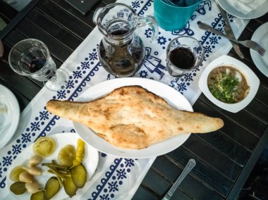 Ekmek. Geleneksel taze pişmiş ekmek koyu ahşap bir masa üzerinde beyaz bir tabak üzerinde yatıyor. Otantik Gürcü ekmeği, kırmızı şarap ve atıştırmalıklar. Ulusal desenli beyaz keten peçete. Gurme Lüks Avrupa.