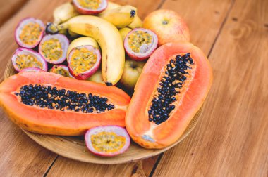 Güzel bir tabak taze sulu tropikal meyve dilimlenmiş papaya, tutku meyveleri, muzlar. Tahta arka planda mükemmel, sağlıklı, egzotik bir yaz kahvaltısı. Düz açıda uzan..