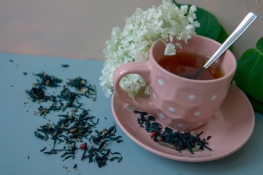 Arka plana karşı bir fincan çay, çiçekler ve ufalanmış çay