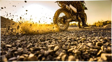 Enduro bir motosikletçi bir yerden başlar ve gün batımına karşı tekerleklerin altından taş atar.
