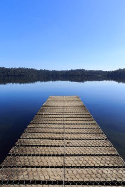 Sabahleyin Yeni Zelanda 'daki sakin ayna gölünde tahta iskele..