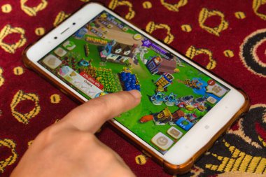Cep telefonu ekranında parmak, bir tarım mobil oyunu oynuyor
