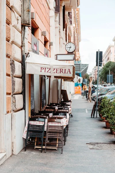 Roma, İtalya - 23 Nisan 2019: Eski kaldırımda damalı bez ve ahşap sandalyelerle kaplı masalar bulunan geleneksel İtalyan sokak restoranı terası. Roma, İtalya.