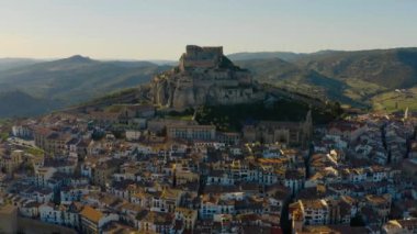 Morella dağının arkasında güneş. Kale, eski evler ve ön planda müstahkem duvarları ile şehir, arka plan olarak gün batımı. Valencia, İspanya.