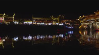 Nehir kenarından Fenghuang gece manzarası. Sokaklarda yürüyen, alışveriş yapanlar ve eğlenen insanlar. Nehir yansıyan ışıklar güzel bir çekim yapar, Hunan eyaleti, Çin.