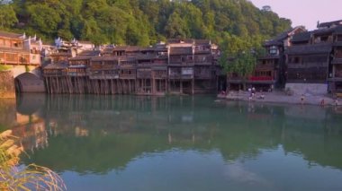 Hunan eyaletinde gün batımında Antik şehir Fenghuang, Çin. İnsanlar nehir kenarında çocuklarla oynarken ve birbirleriyle konuşurlar.
