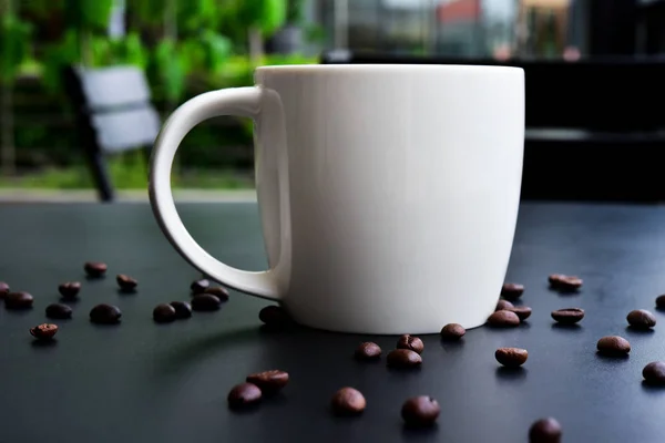 गडद लाकूड टेबलवर कॉफीच्या कॅपमध्ये बरेच कॉफी बीन्स आहेत . — स्टॉक फोटो, इमेज