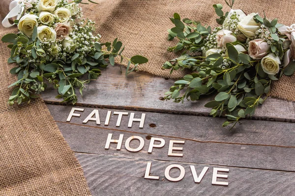 Rustic background with bouquets and burlap with the words Faith, Hope and Love spelled out in wooden letters