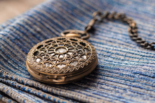 Pocket watch sitting on top of a blue clothe. The time is 3:49.
