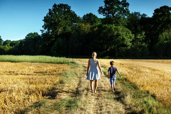 Mother and son walking on path in field; France