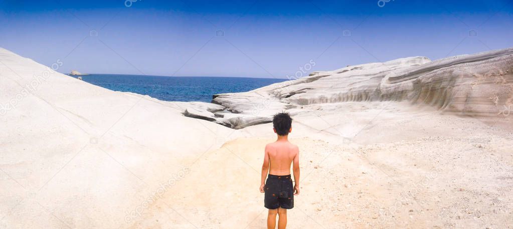 Boy standing on white rock and admiring sea 