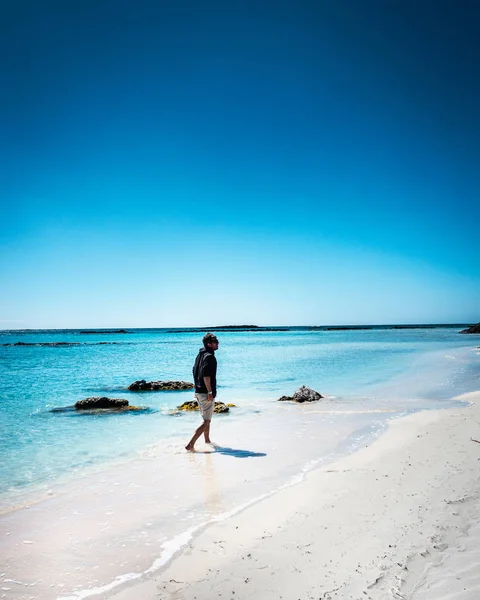 Jonge man lopen op het strand met handen in zak — Stockfoto